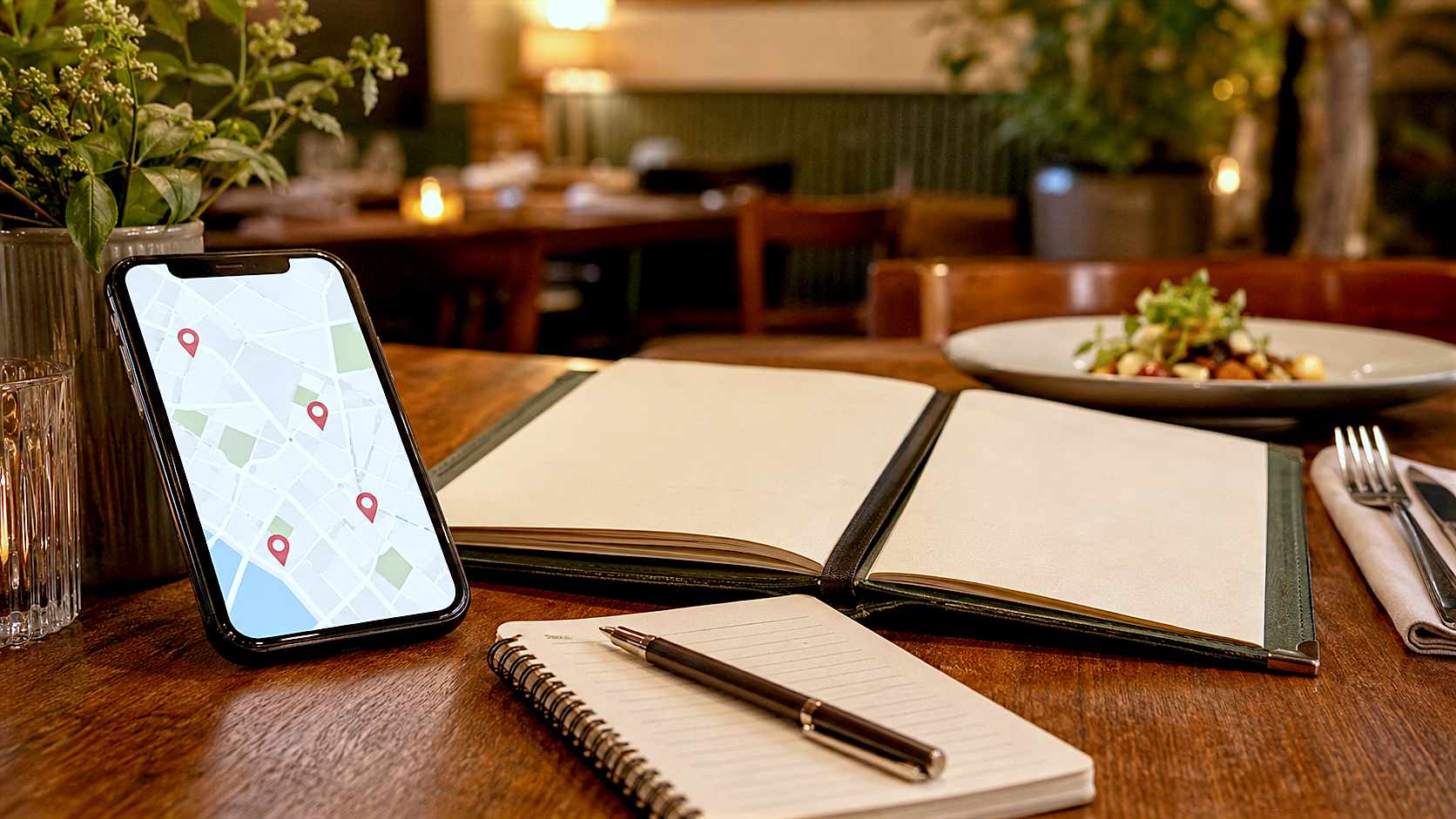 Restaurant table with a smartphone map, open menu and notebook ready for comparing dining options.