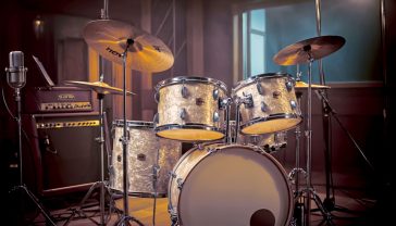A hyper-realistic, professional photograph in the style of a Mojo magazine feature. The image shows a vintage 1960s Ludwig drum kit with an oyster pearl finish, set up in a classic British recording studio reminiscent of Abbey Road. Soft, warm light comes from one side, highlighting the texture of the drumheads and the gleam of the cymbals. In the background, vintage microphones and sound-proofing panels are softly out of focus. The mood is nostalgic, professional, and deeply connected to British music heritage.