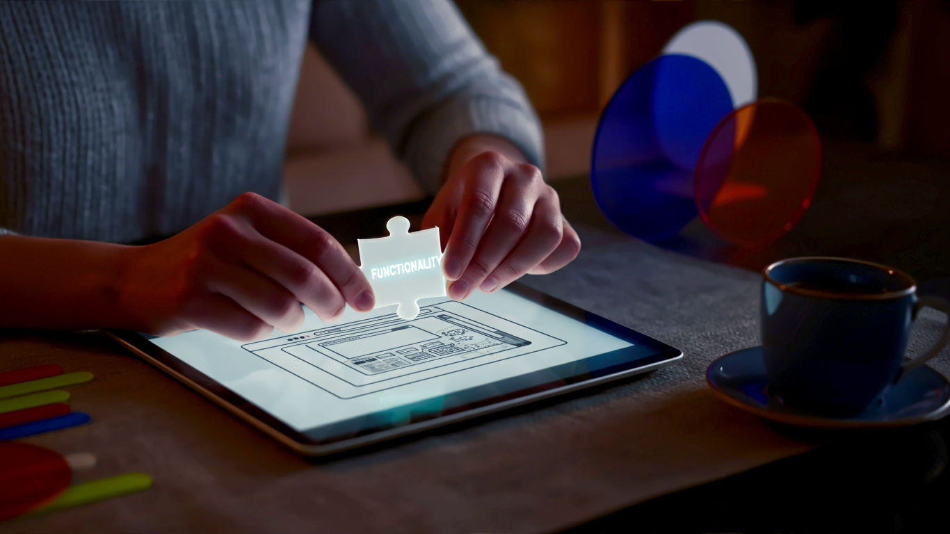 A hyper-realistic, professional photograph showing a person's hands adding a glowing, jigsaw puzzle piece labelled 'Functionality' into a sleek, modern website blueprint on a tablet. The background is a cosy but professional British home office, with a cup of tea visible. The mood is empowering and creative, with soft, natural lighting.