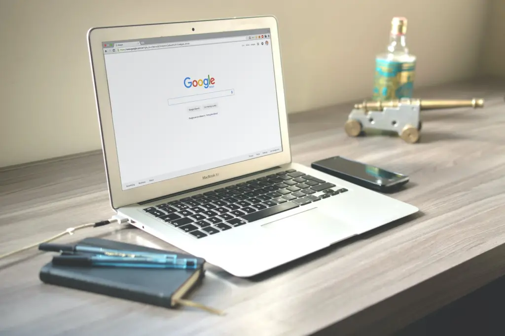 Search Engines | A Macbook Air sits atop a desk with the Google homepage open, awaiting input.