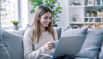 A hyper-realistic, professional photograph in the style of a modern lifestyle magazine. The image captures a cheerful and savvy British woman in her late 20s, sitting on a comfortable sofa in a bright, contemporary living room with a cup of tea. She is smiling, looking at her laptop screen which displays a colourful, well-designed online shop at the checkout stage, with a voucher code successfully applied, showing a "Discount Applied!" message. The composition is a medium shot, with soft, natural lighting from a nearby window. The mood is positive, empowering, and relatable, evoking the quiet satisfaction of smart online shopping.