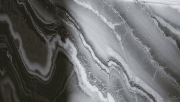 Close-up photograph of premium granite slab with dramatic white and grey veining, captured under natural lighting to highlight its crystalline sparkle and translucent qualities. The image should show the stone's surface at an angle that reveals its depth and dimension, with a soft-focus kitchen environment visible in the background.
