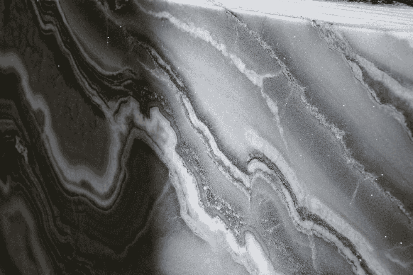 Close-up photograph of premium granite slab with dramatic white and grey veining, captured under natural lighting to highlight its crystalline sparkle and translucent qualities. The image should show the stone's surface at an angle that reveals its depth and dimension, with a soft-focus kitchen environment visible in the background.